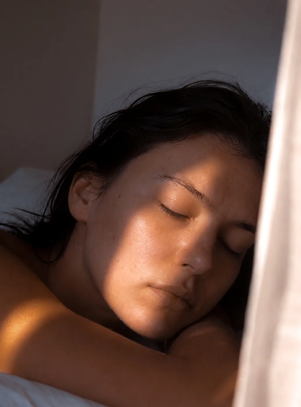 Une femme endormie, le visage traversé par la lumière chaude de l'aube